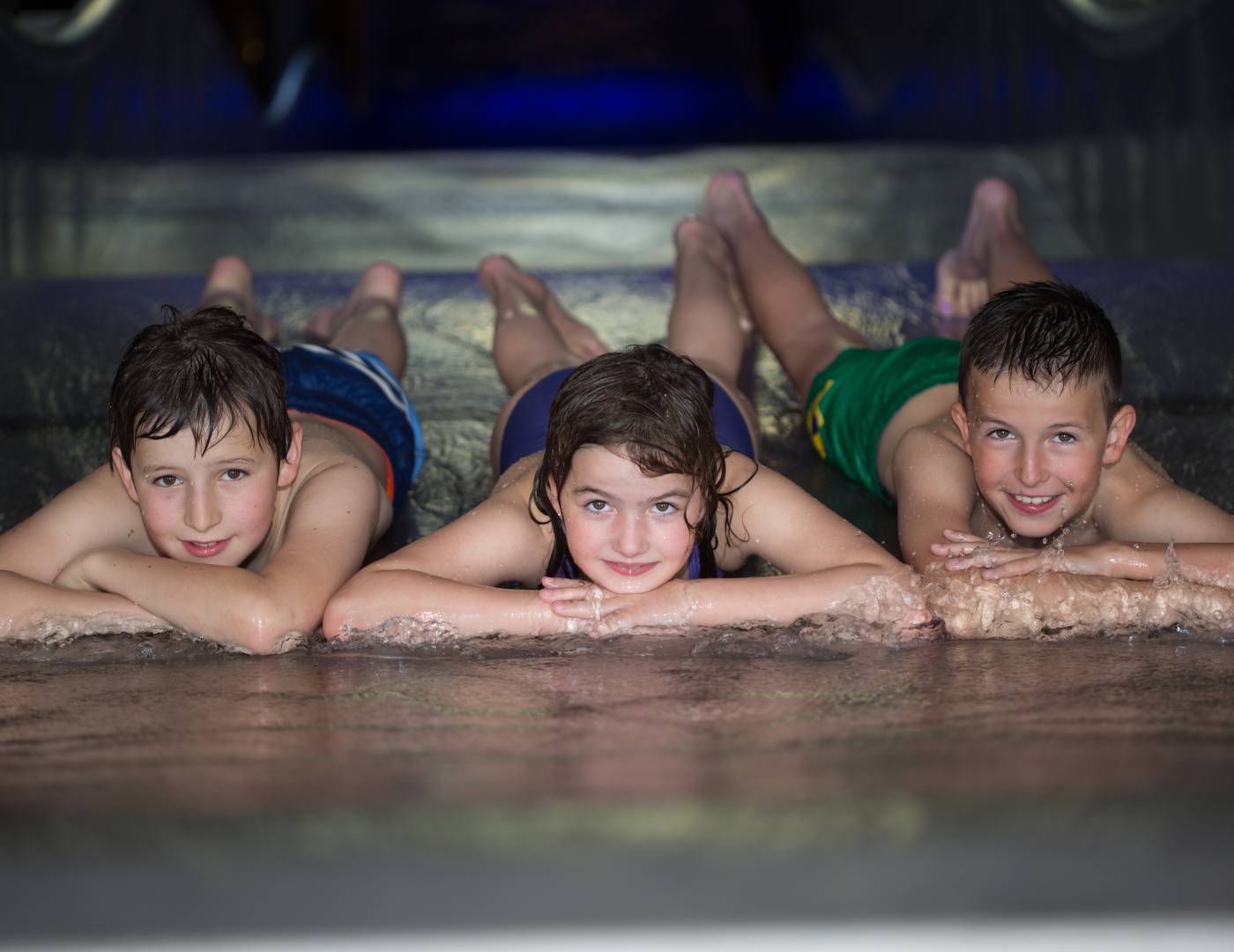 Three children lying and laughing on the waterslide at the family hotel