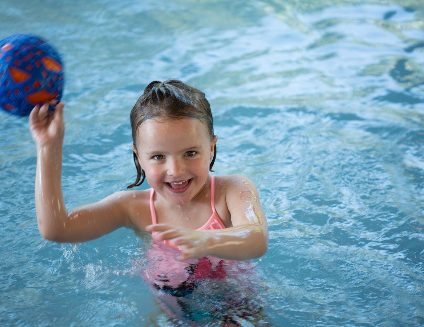 Mädchen mit Ball im Kinder-Schwimmbad des Familienhotels