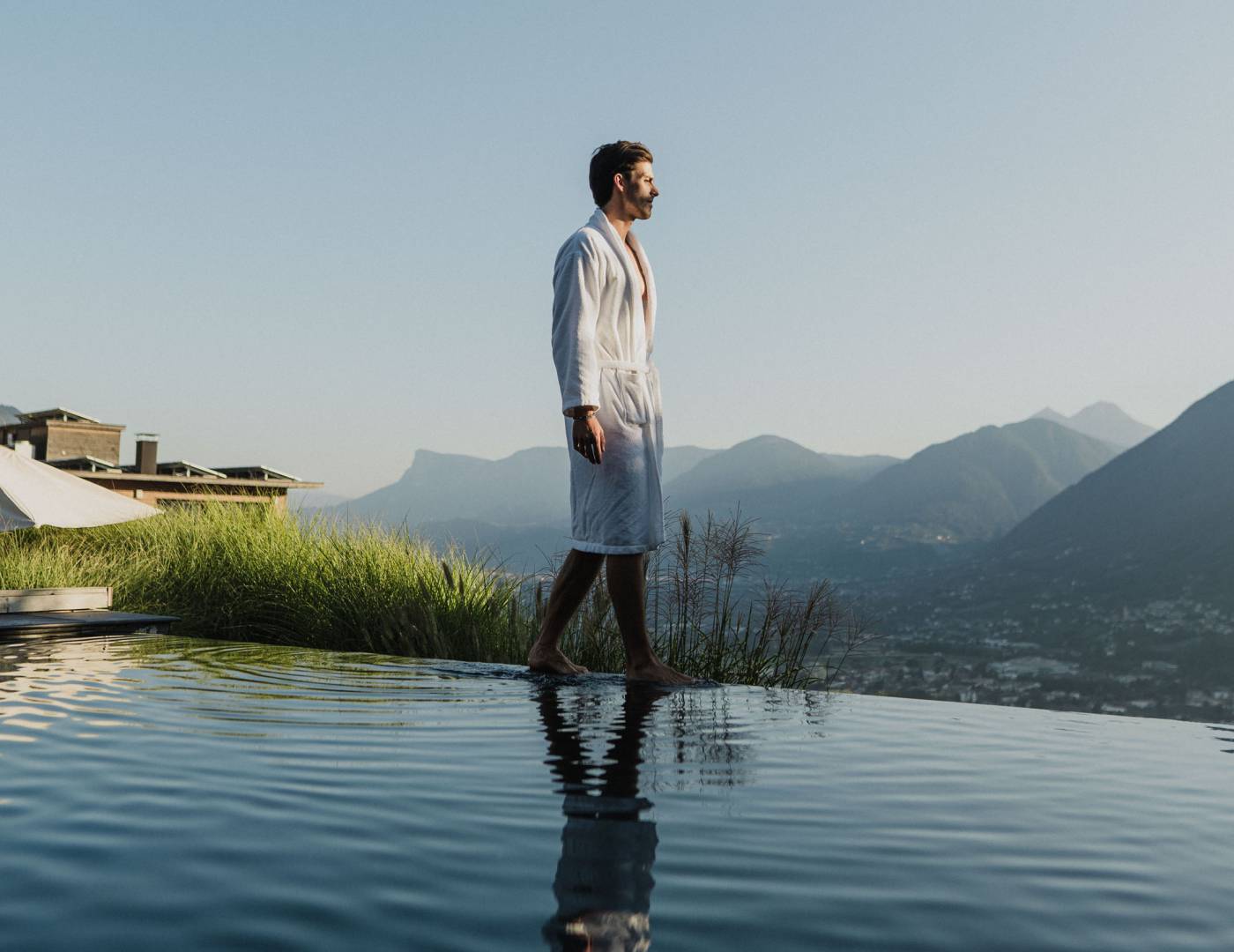 Man in a bathrobe walking along the infinity pool of a 5-star wellness hotel in Merano, South Tyrol