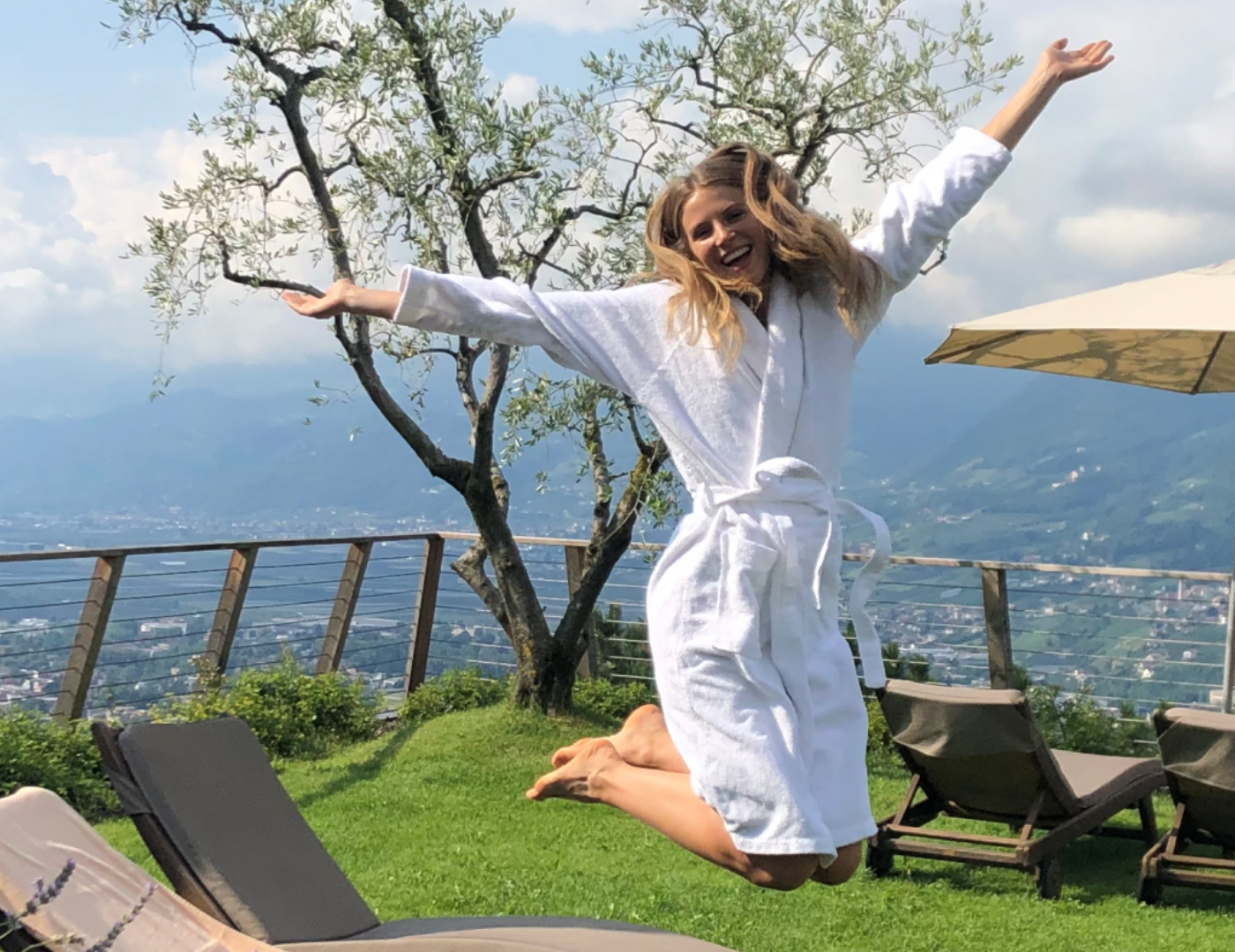 Donna sorridente in accappatoio che salta sulla terrazza dell’hotel benessere a Tirolo
