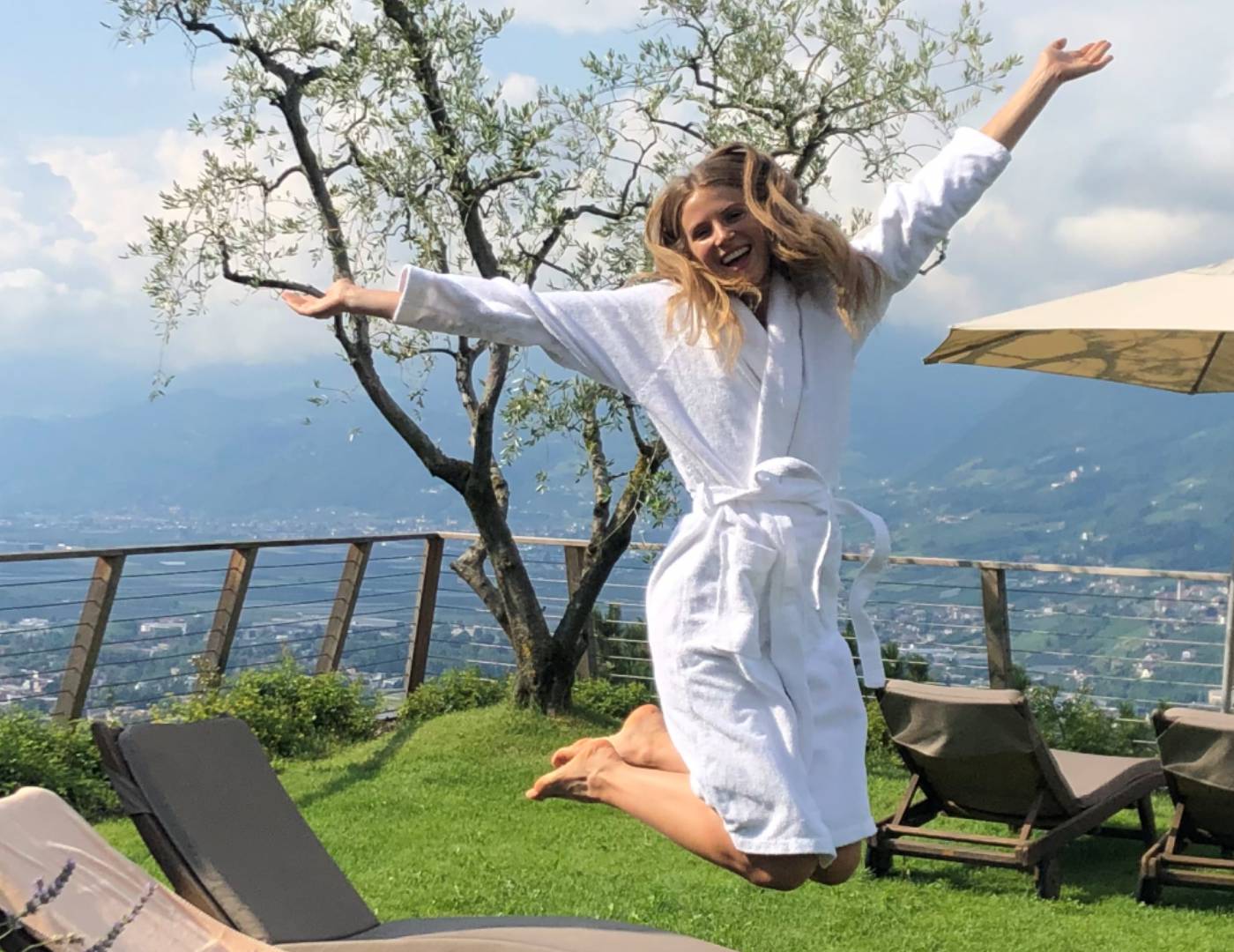 Donna sorridente in accappatoio che salta sulla terrazza dell’hotel benessere a Tirolo