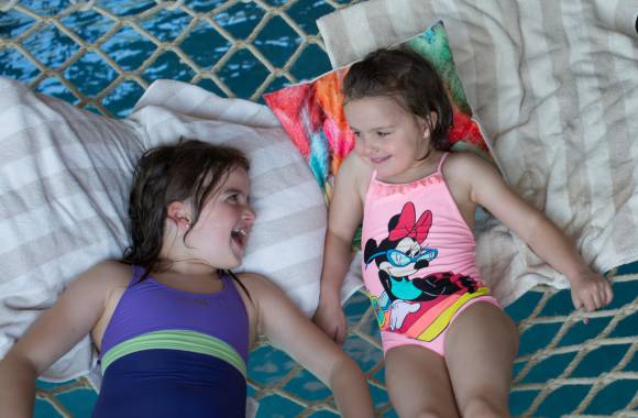 Zwei Mädchen entspannen in der Hängematte im Kinderschwimmbereich des Familienhotels in Südtirol