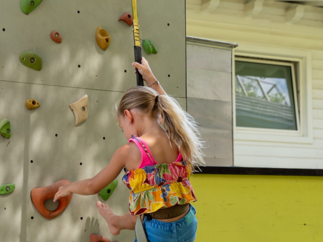 Mädchen klettert an der Kletterwand im Außenspielbereich des Kidsclubs eines Familienhotels in Südtirol
