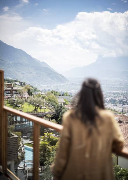 Frau auf Balkon mit Blick auf Hotel Erika und Meran